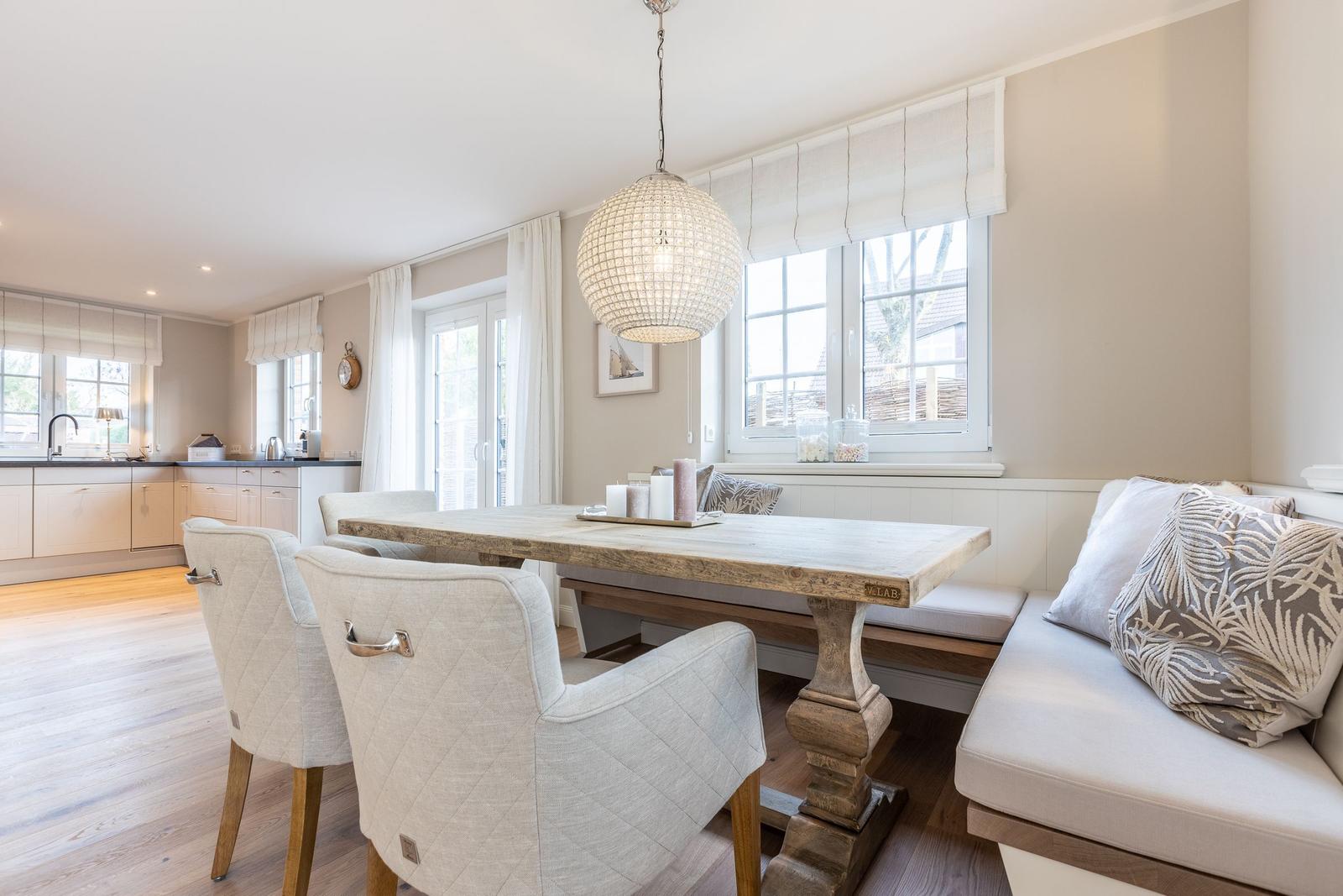 Dining area with wooden table, bench, and chairs. Kitchen area in background.