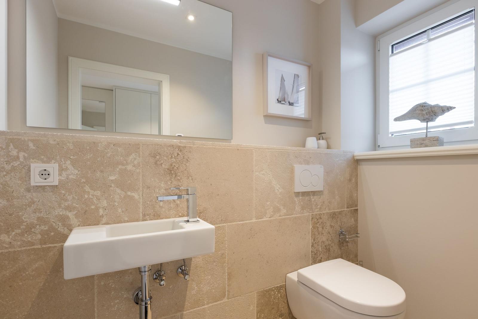 Bathroom with sink, mirror, and toilet. Window with shell decoration.