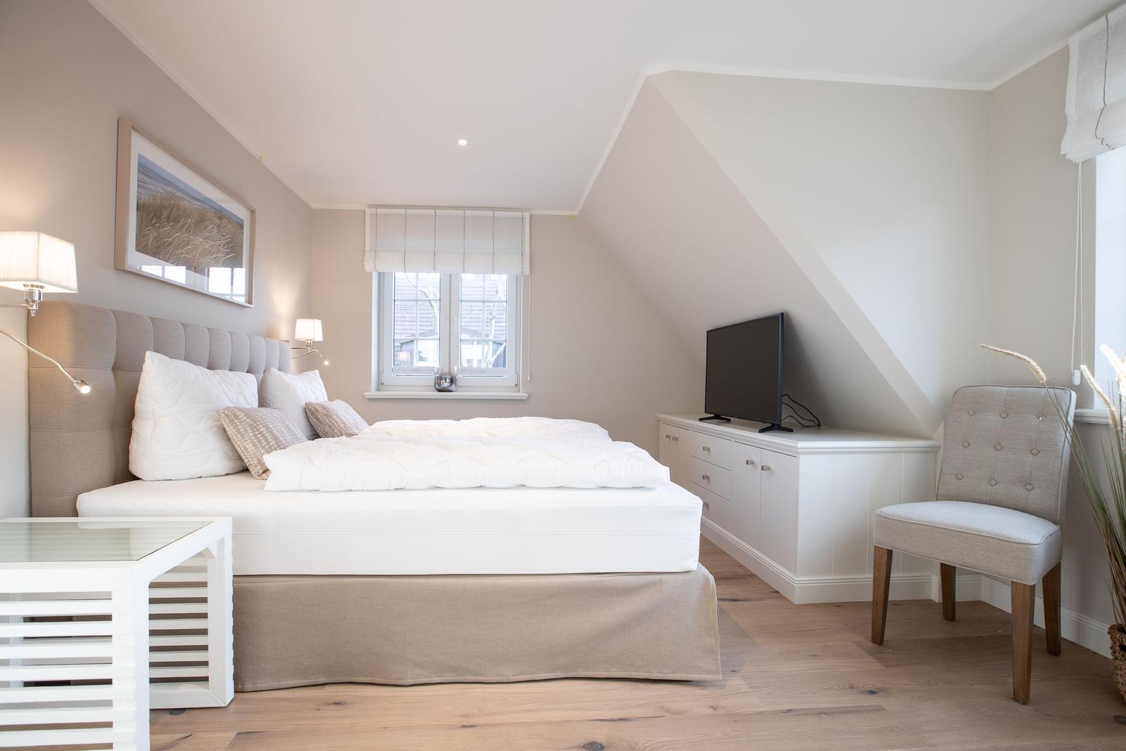 Bedroom with sloped ceiling, bed, TV, and chair.