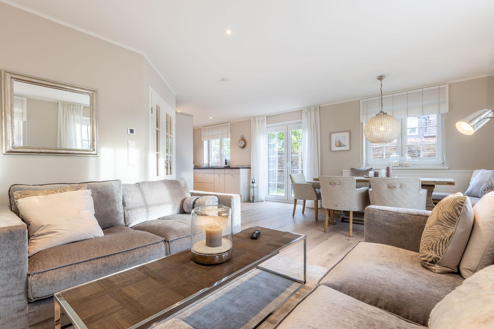 Living and dining area with sofa, table and chairs. Windows with curtains and ceiling light.