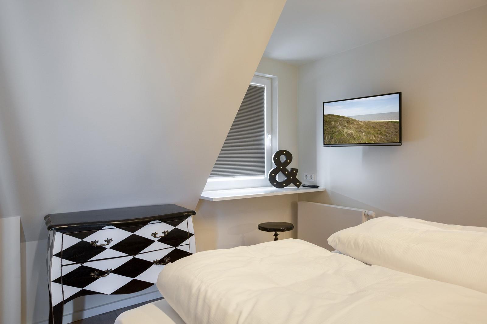 Schlafzimmer mit Doppelbett, schwarz-weißem Schrank und Wandfernseher.