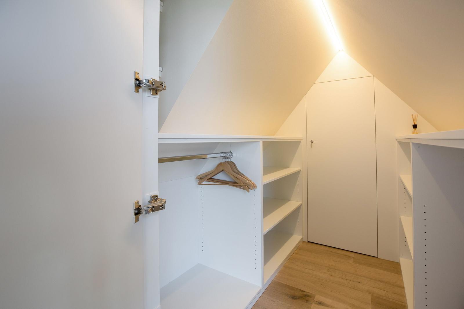 Kleiderschrank mit Haken und Regalen unter schräger Decke.