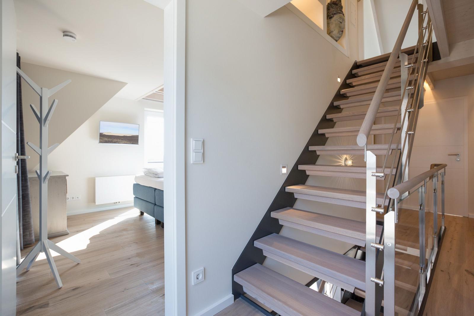 Treppe mit Holzstufen und Metallgeländer führt zu einem Schlafzimmer mit Bett und Kleiderständer.