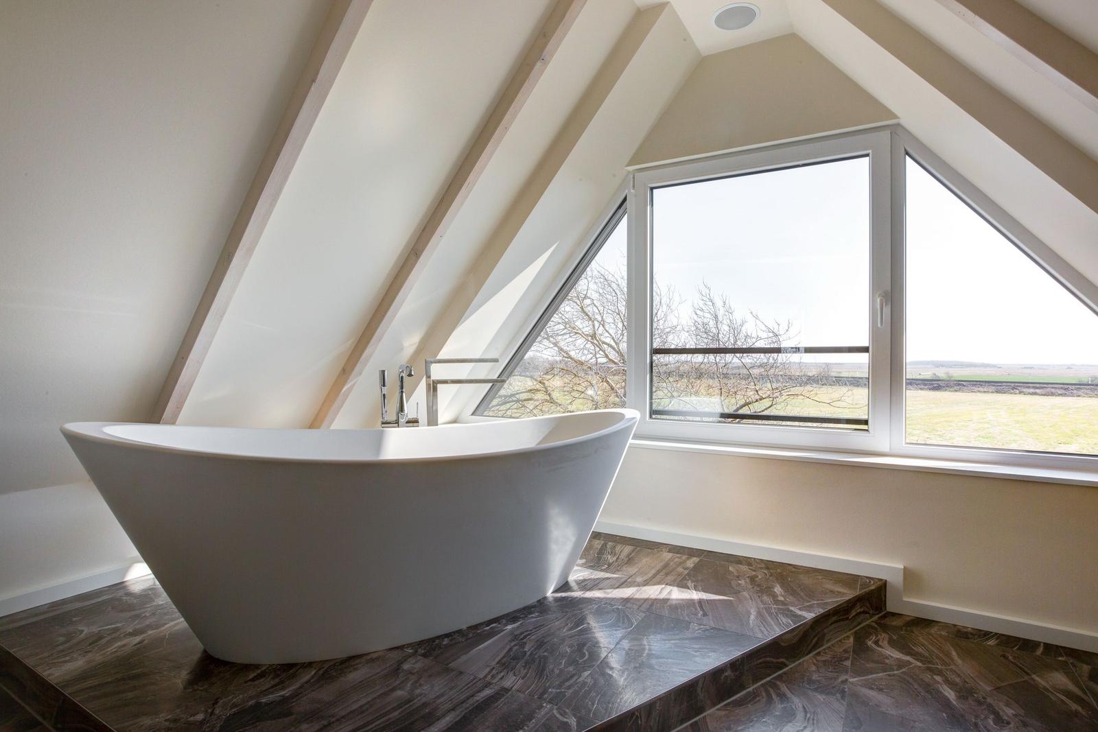 Freistehende Badewanne unter Dachschrägen mit großem Fensterblick auf Landschaft