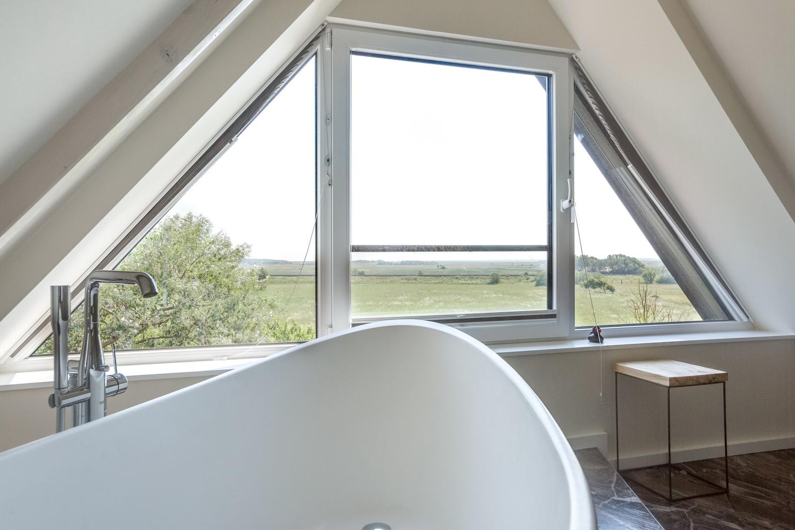 Badewanne mit Blick auf grünes Feld durch Dachfenster