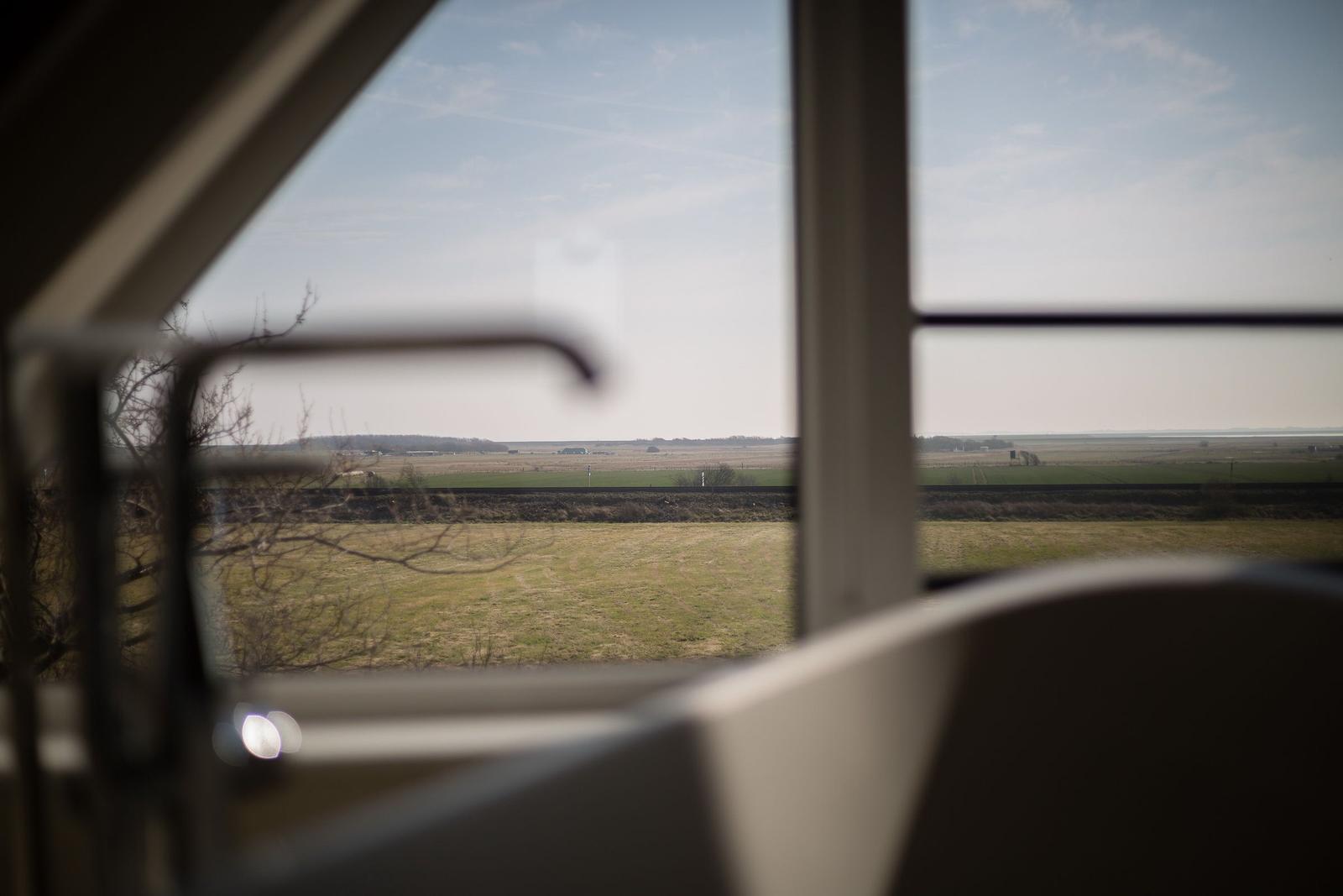 Durch das Fenster blickt man auf eine weite Landschaft mit Feldern und Bäumen.
