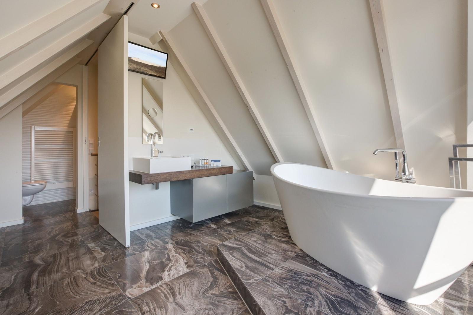 Badezimmer mit freistehender Badewanne, Waschbecken und Toilette unter Dachschrägen.