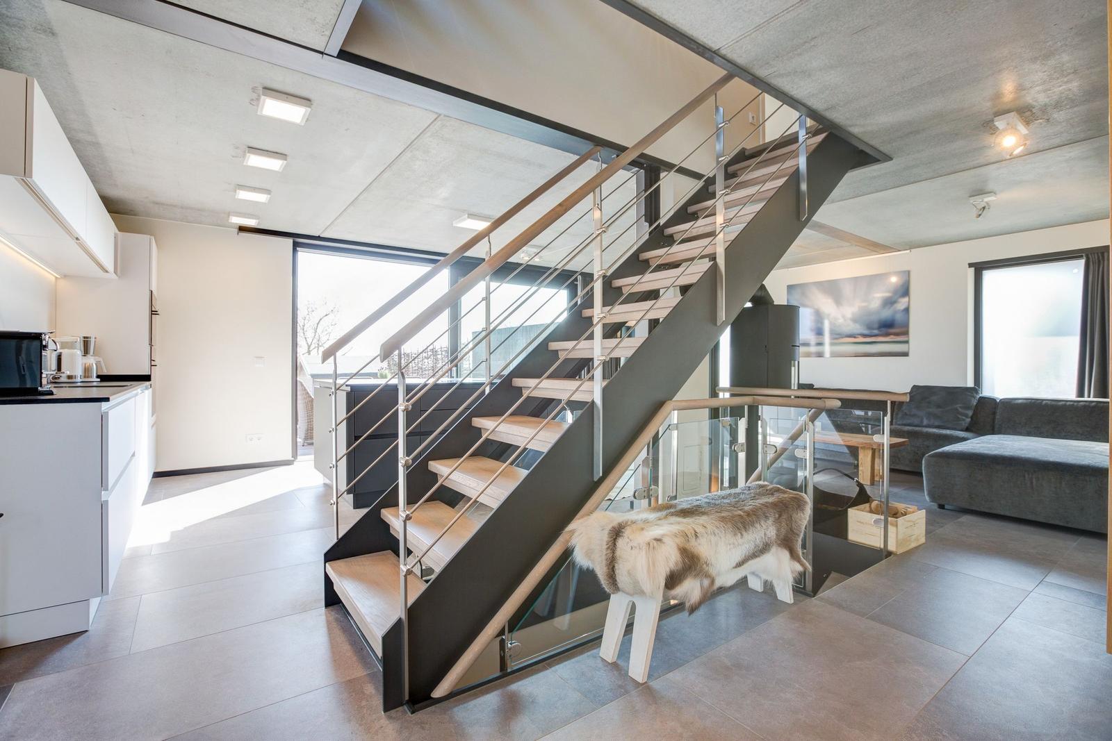 Moderne Wohnung mit Holzstufen und Glasgeländer. Küche, Wohnbereich und Fenster sichtbar.