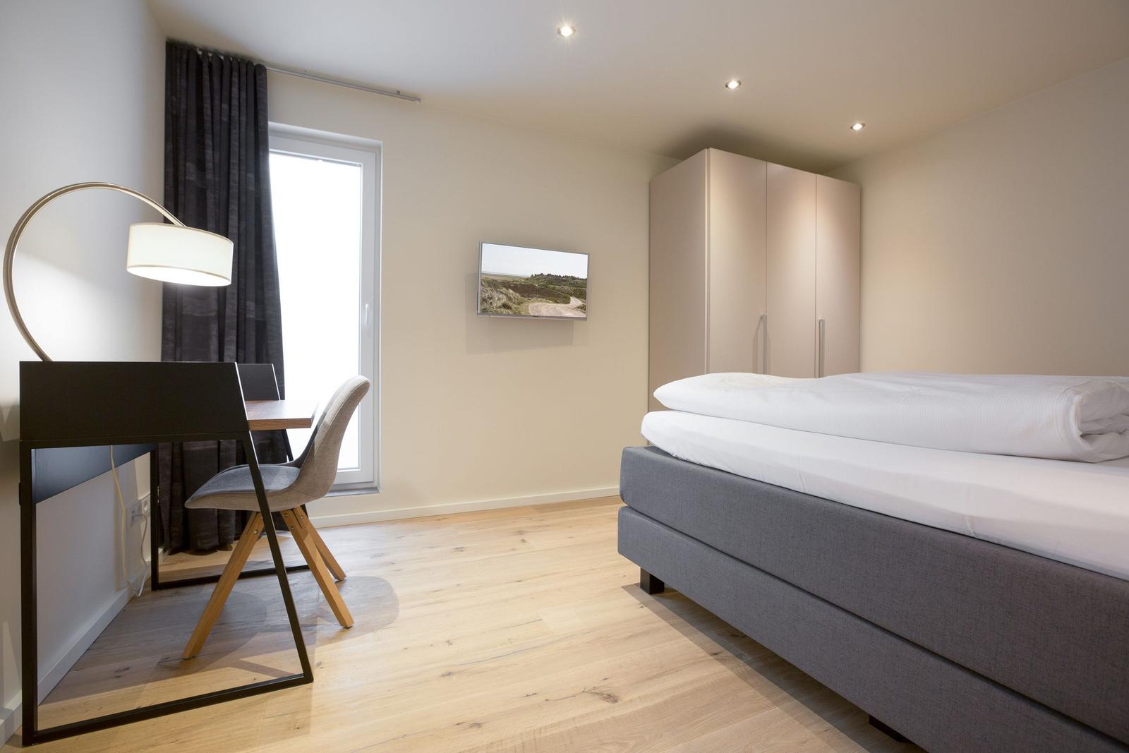 Schlafzimmer mit Bett, Schreibtisch und Kleiderschrank.