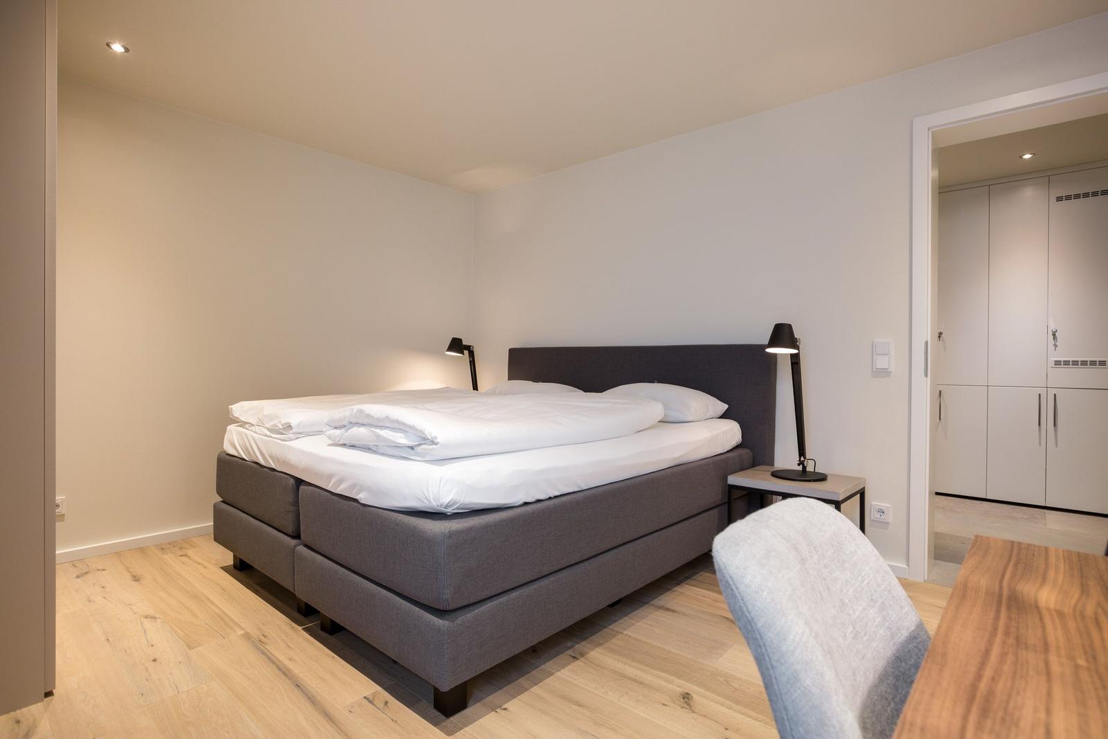 Schlafzimmer mit Bett, Nachttisch und Lampe. Durchgang zu einem Schrankraum.