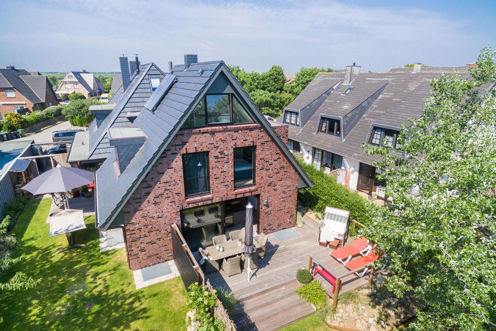 Modernes Haus mit Holzterrasse, Garten und Sonnenliegen.