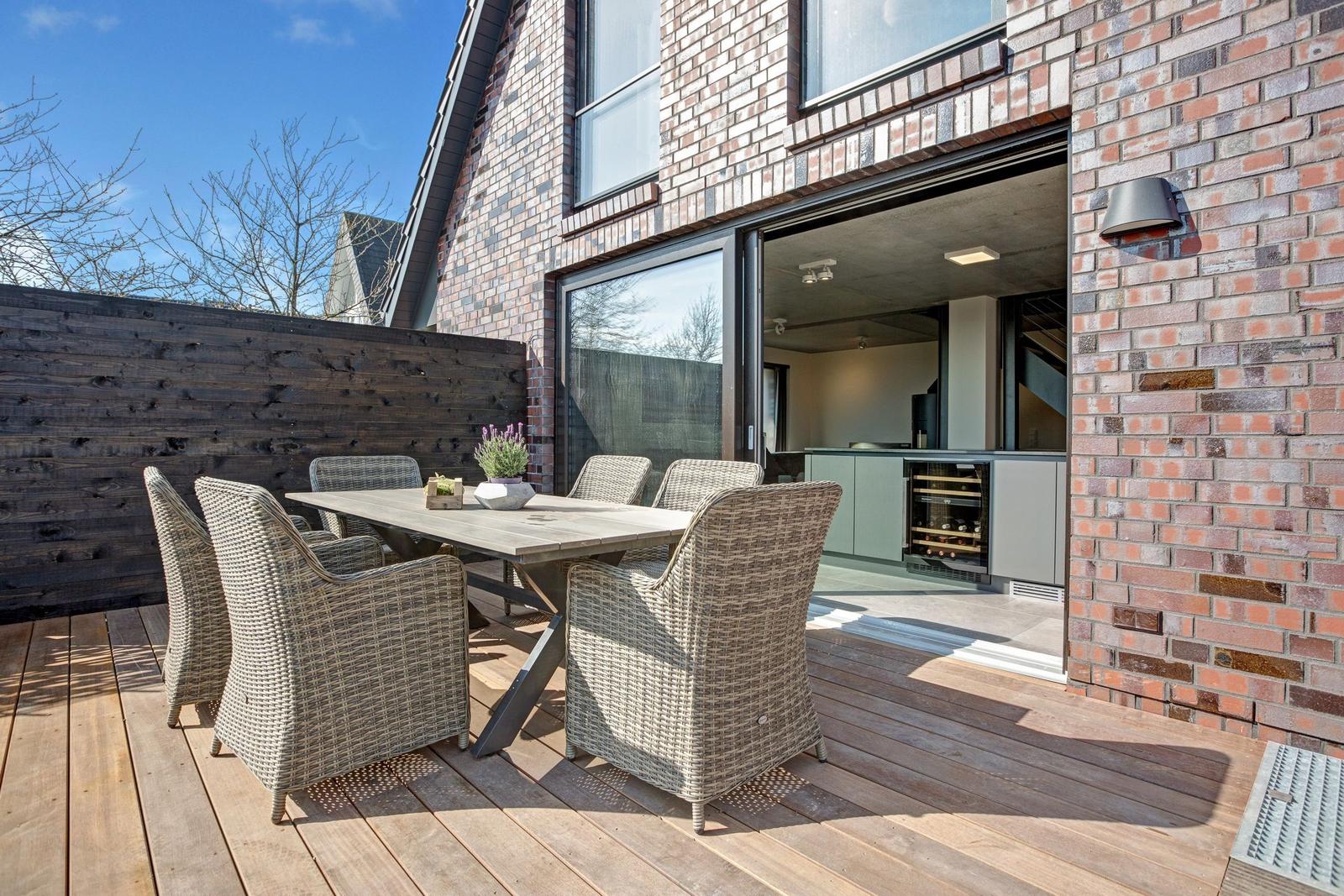 Terrasse mit Holzdecke und Sitzgruppe. Durchgang ins Haus mit Küchenbereich.