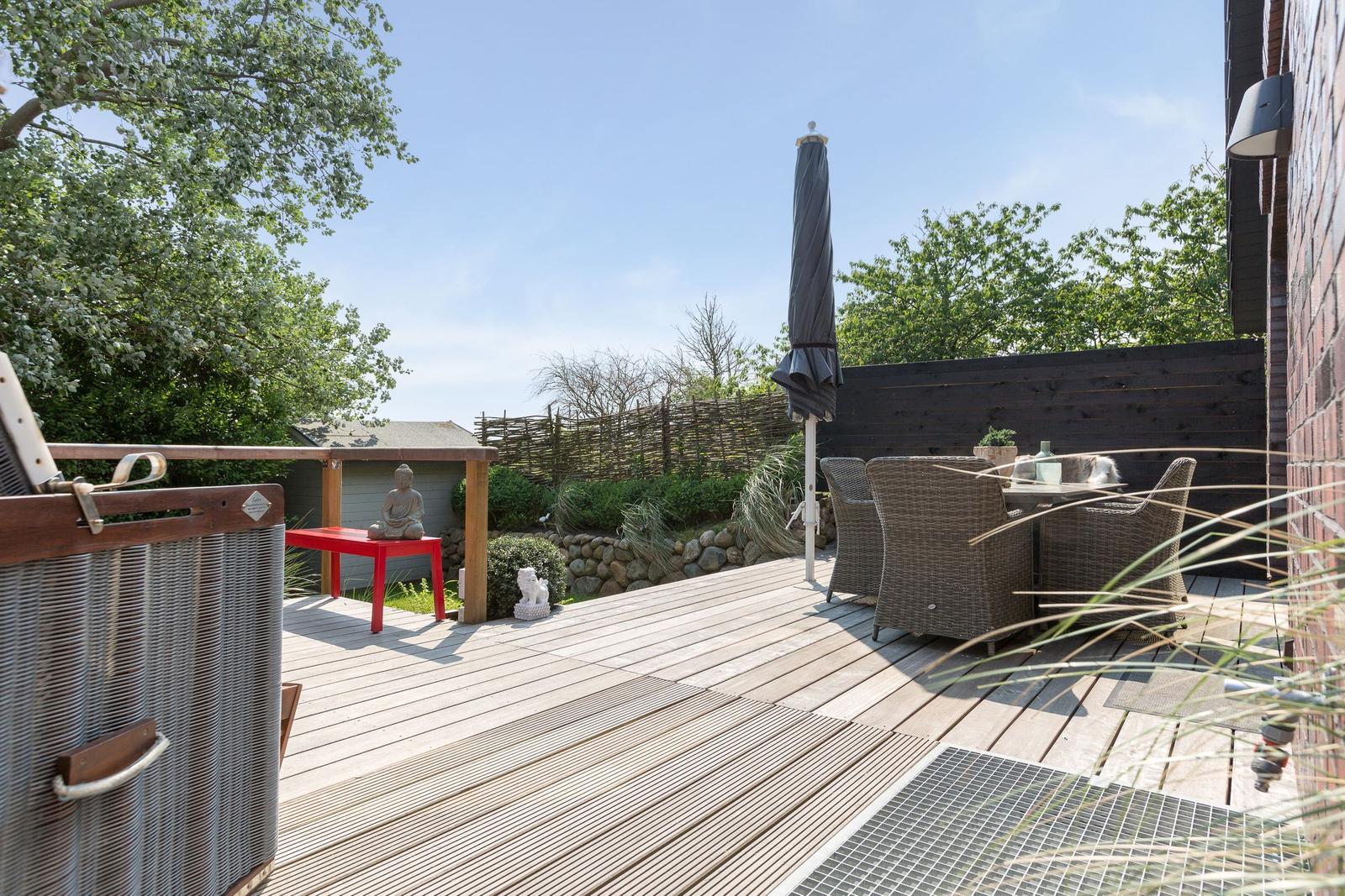 Terrasse mit Gartenmöbeln, Sonnenschirm und Holzdecke.