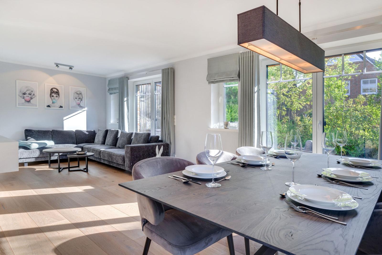 Esszimmer mit Tisch und Stühlen. Wohnbereich mit Sofa und Fenstern.