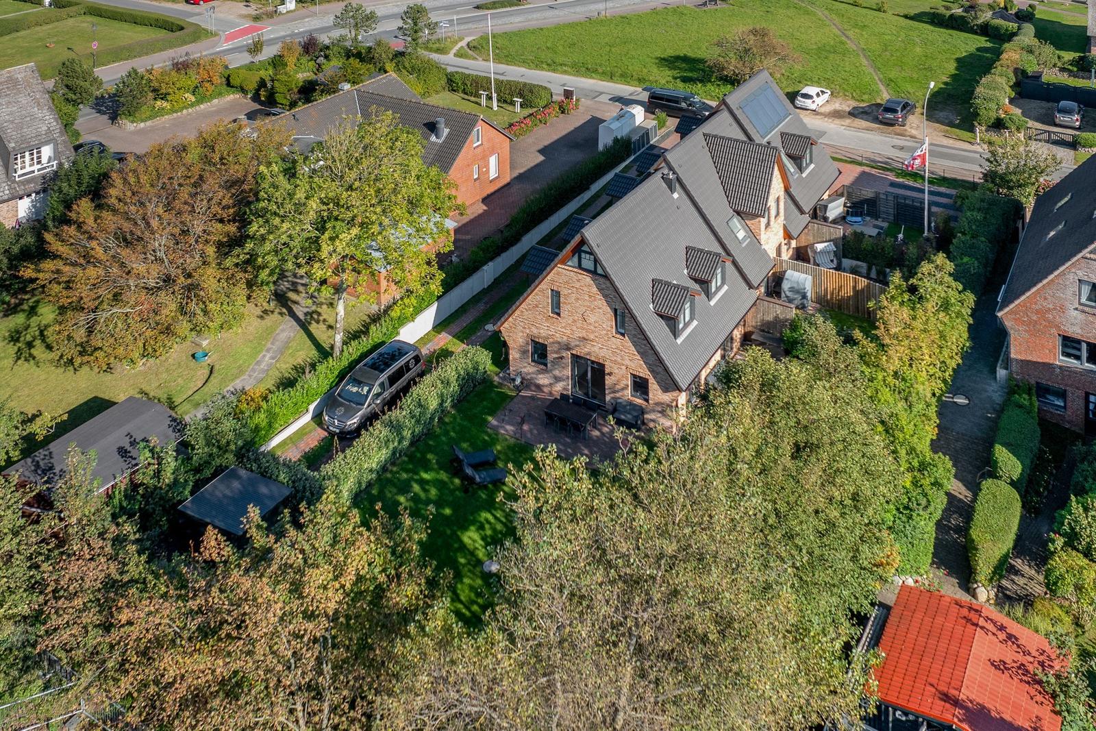 Haus mit Garten und Terrasse, umgeben von Bäumen und Grünflächen.