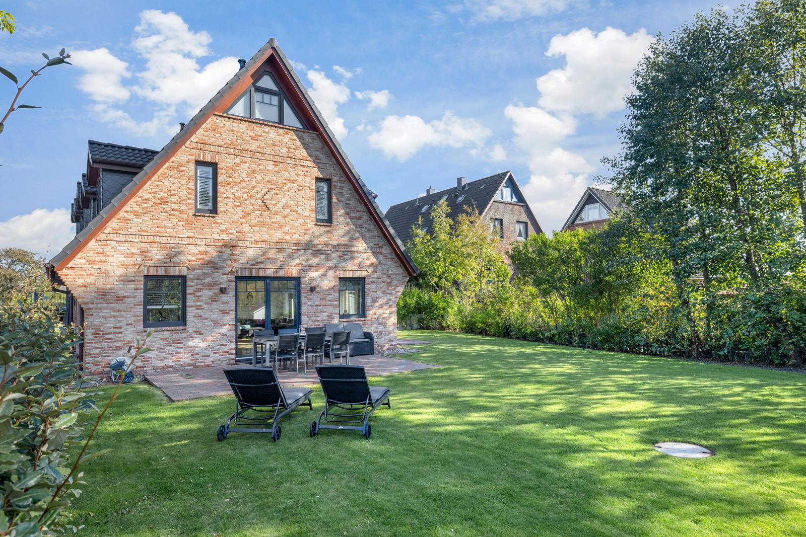 Haus mit Garten, Liegestühlen und Terrasse unter blauem Himmel.