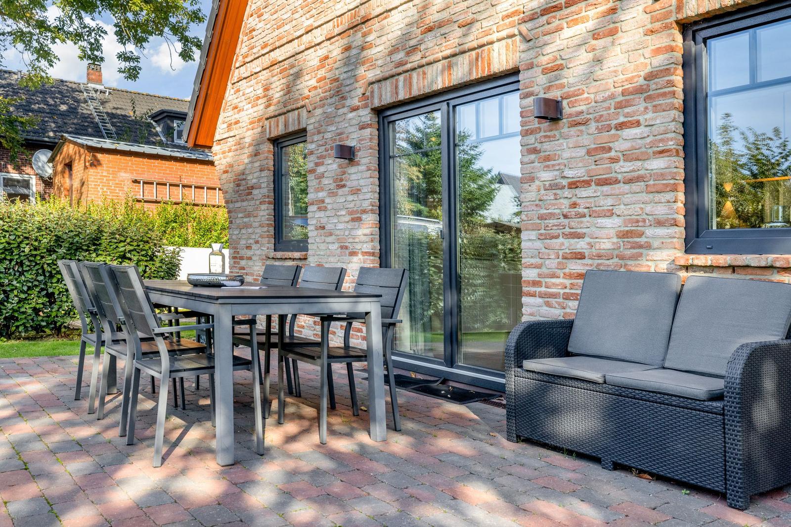 Terrasse mit Tisch, Stühlen und Sofa vor Backsteinhaus.
