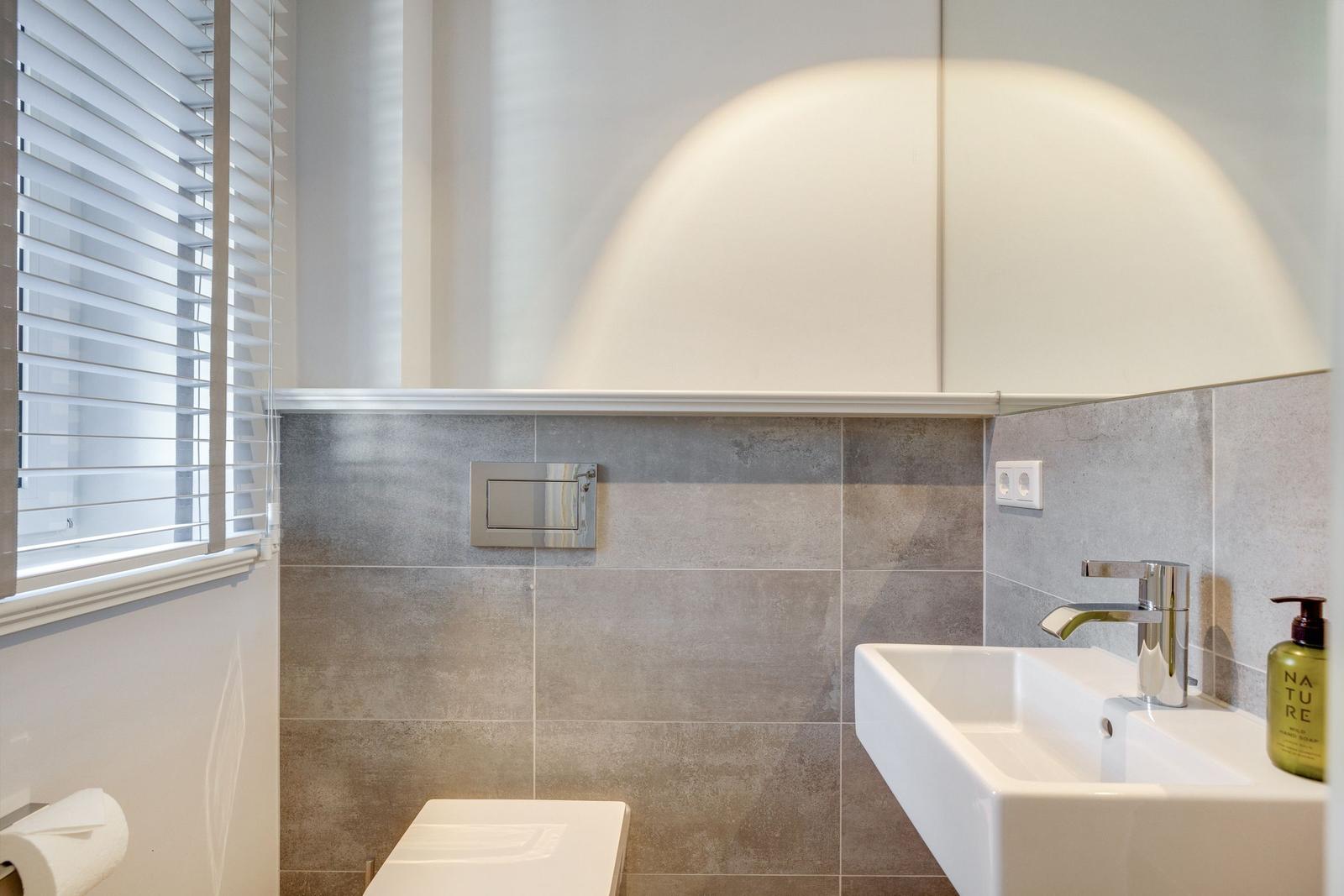 Badezimmer mit Waschbecken, Toilette und Fenster mit Jalousie.