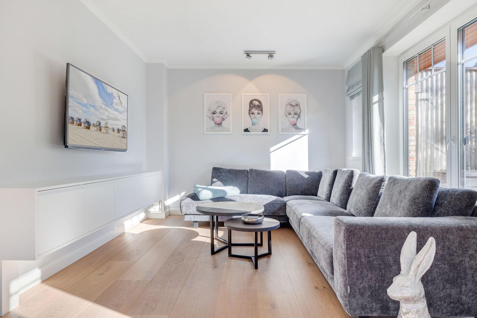 Wohnzimmer mit grauem Sofa, Fernseher und drei Wandbildern.