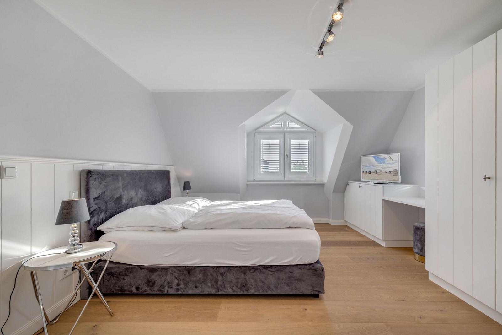 Schlafzimmer mit Dachschrägen, Bett, Schreibtisch und Kleiderschrank.