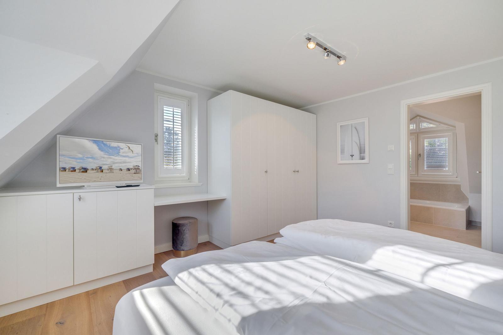 Schlafzimmer mit Bett, Kleiderschrank und TV. Durchgang zur Badewanne.