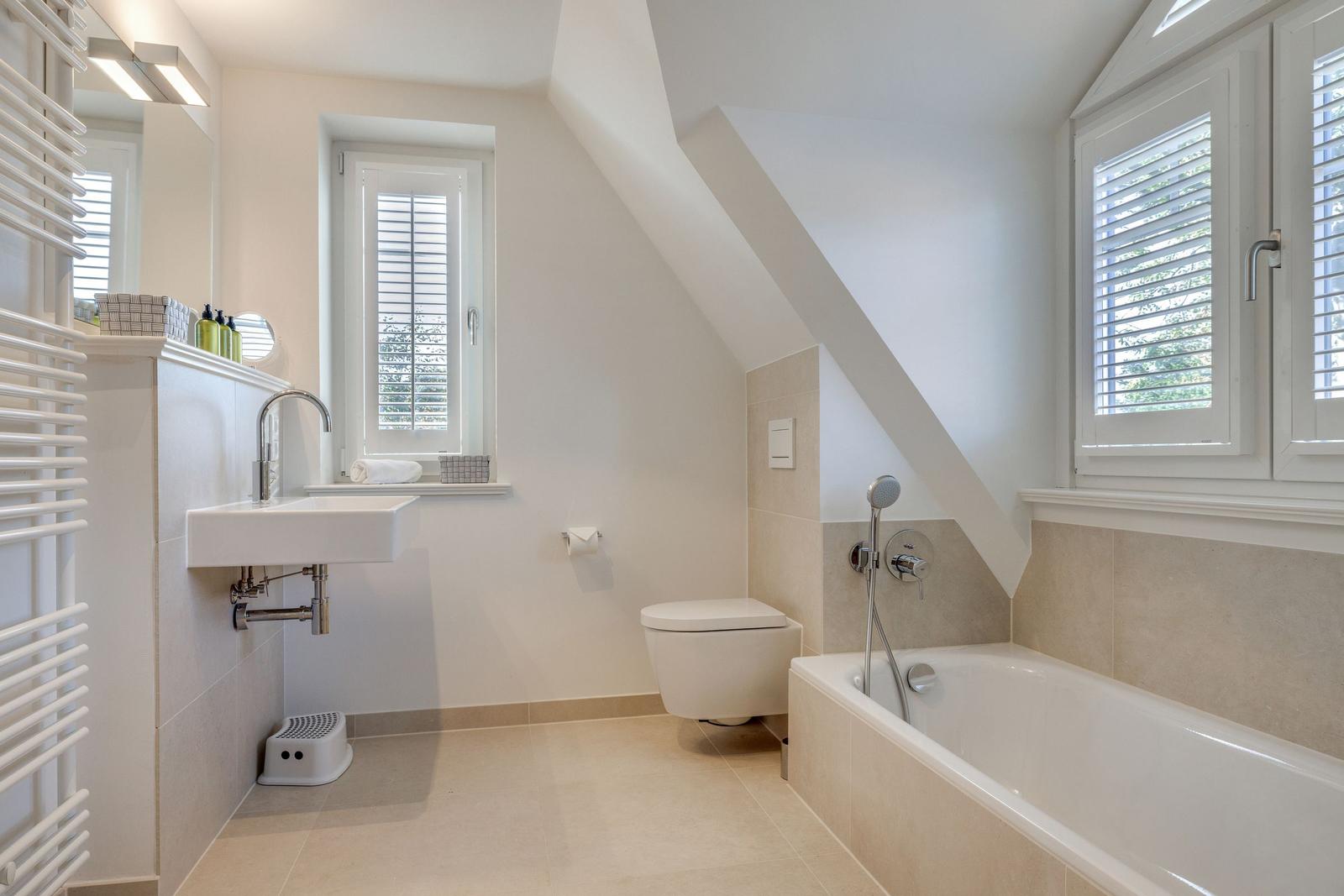 Badezimmer mit Badewanne, Toilette und Waschbecken unter Dachschrägen.