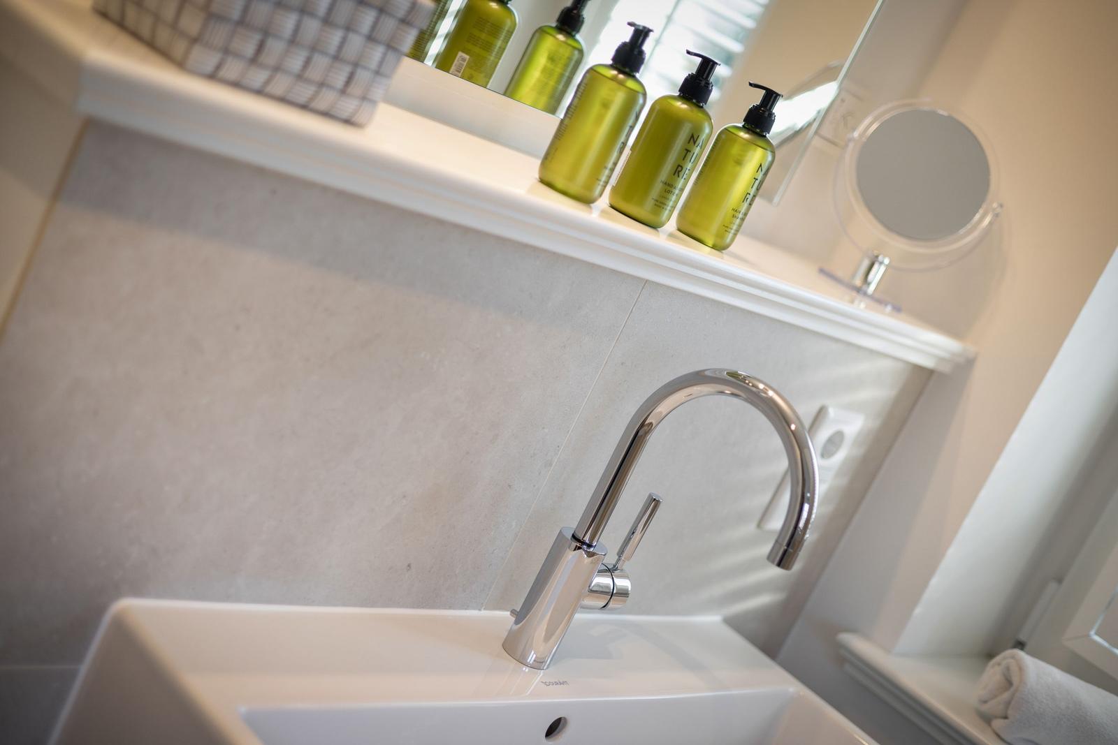 Waschbecken mit modernem Wasserhahn und grünen Flaschen auf der Ablage.