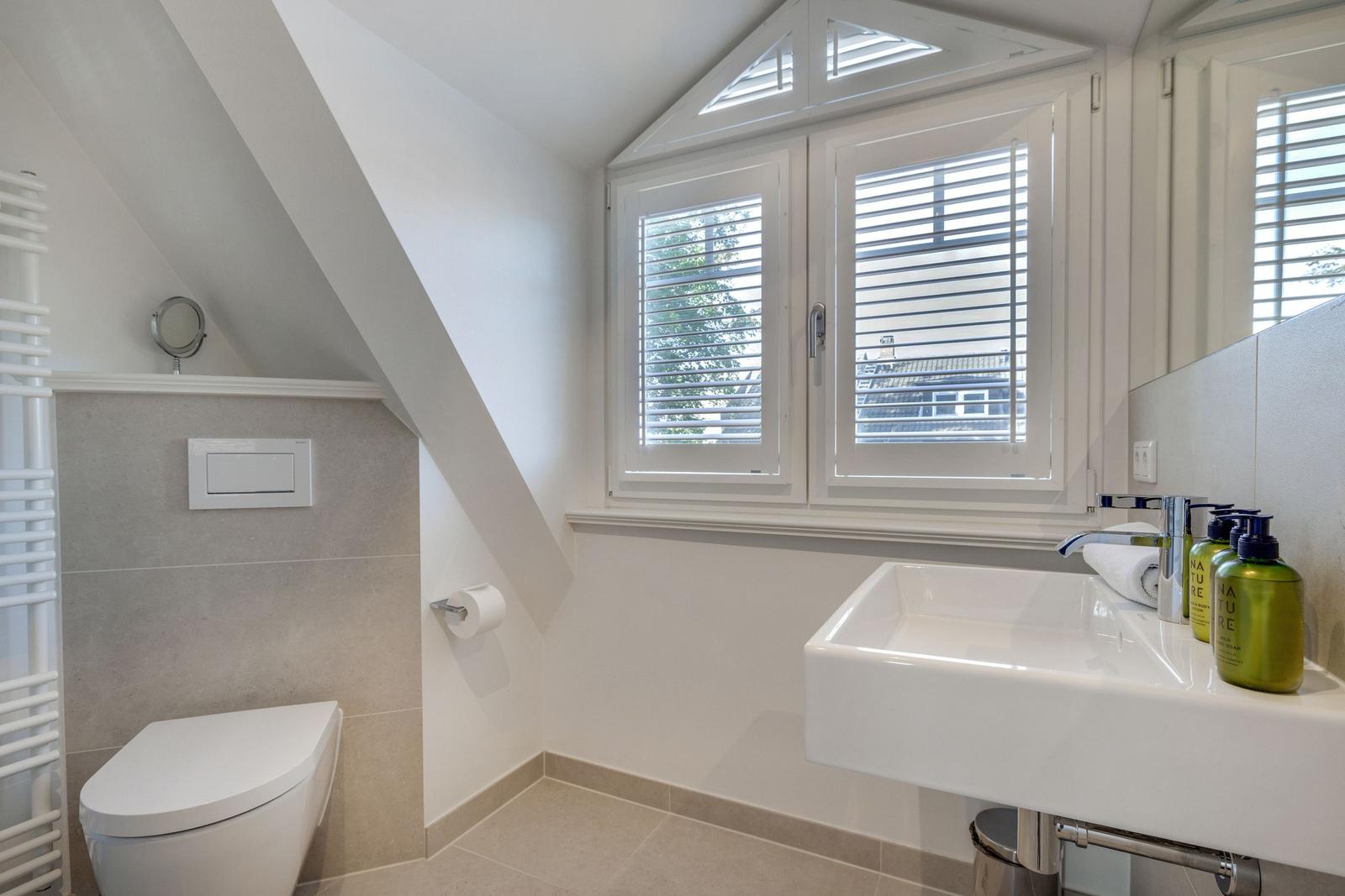 Badezimmer mit Toilette, Waschbecken und Fenster mit Jalousien.