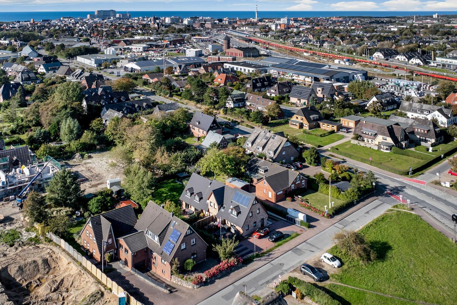 Aerial view of residential area near sea with houses, roads, and industrial zones visible.