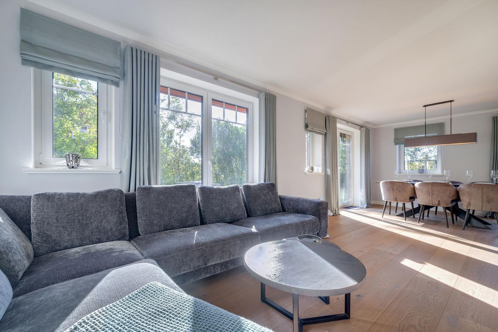 Wohn- und Essbereich mit grauem Sofa, Holzboden und großen Fenstern.