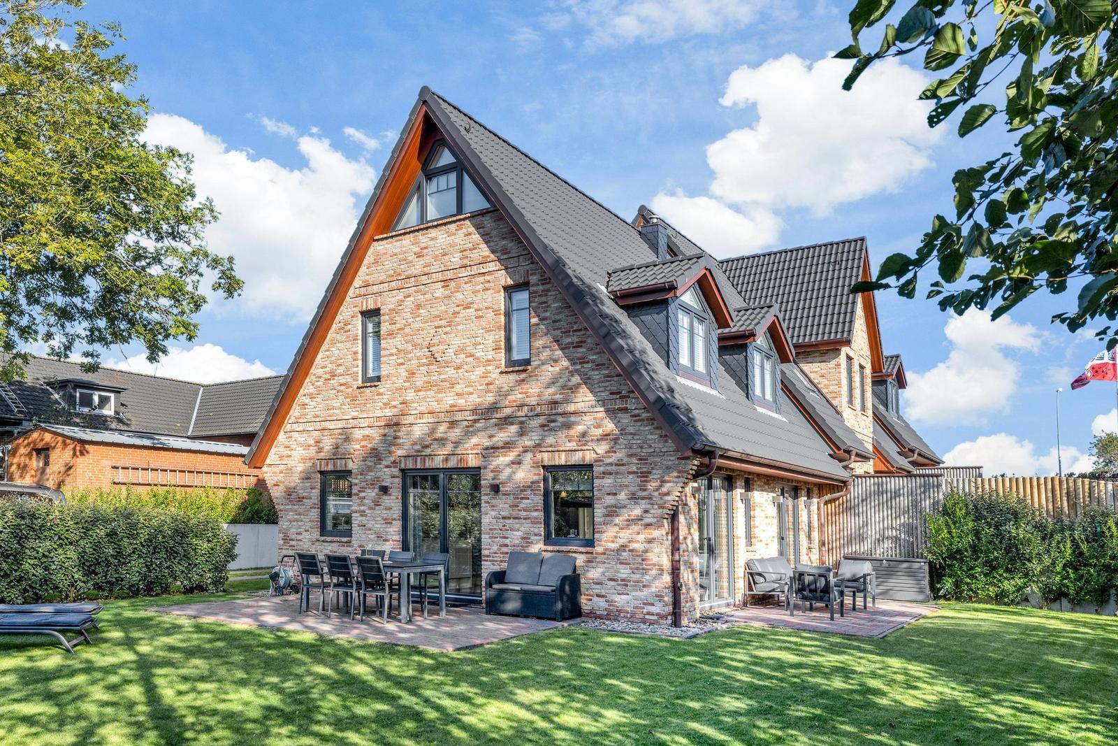 Ferienhaus mit Backsteinfassade, Terrasse und Garten unter blauem Himmel.