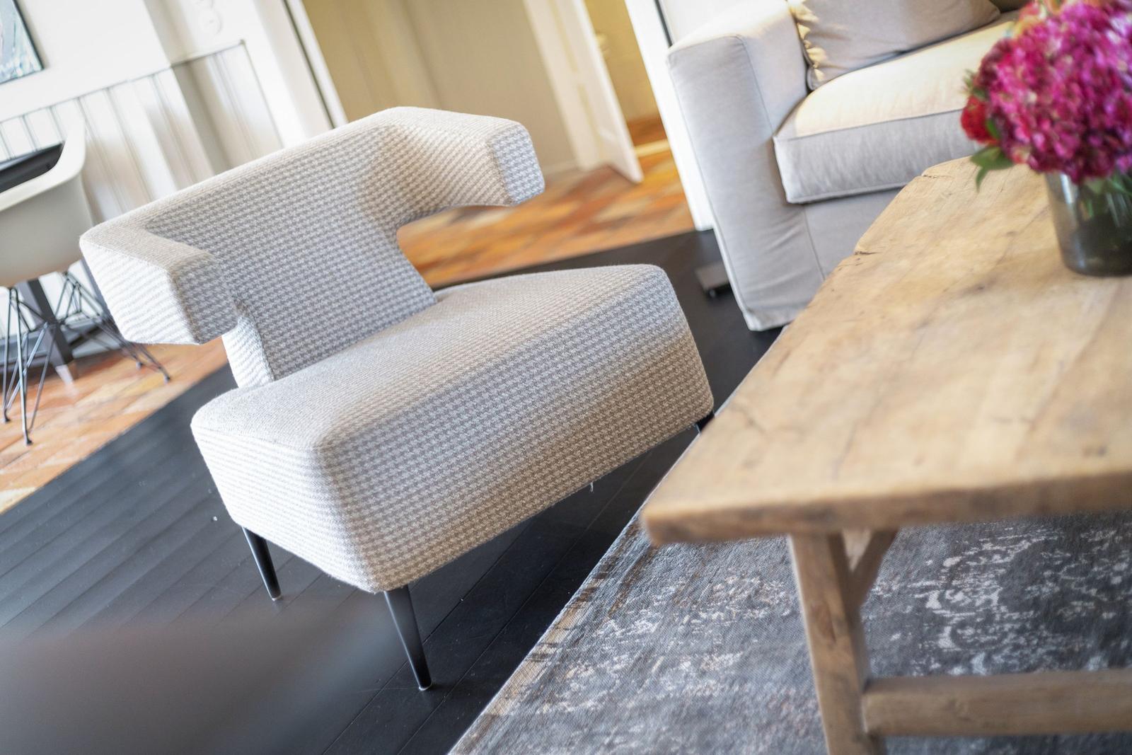 Ein Sessel mit gemusterter Bezugsstoff und schwarzen Beinen steht neben einem Holztisch.