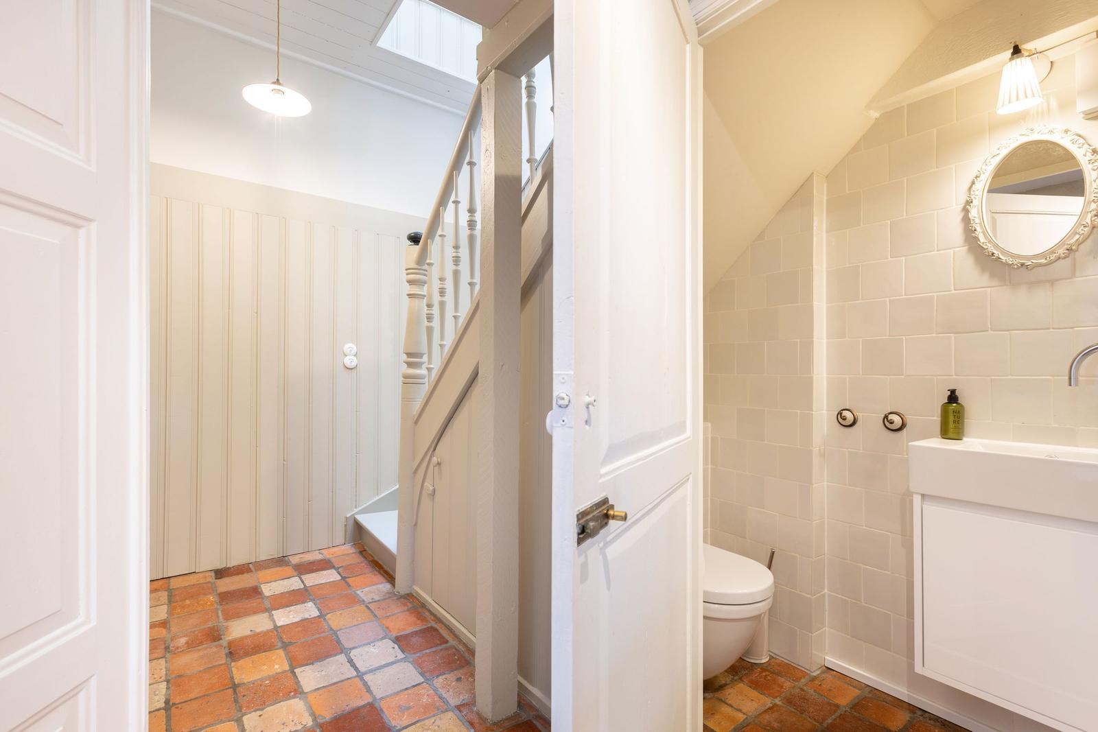 Badezimmer mit Toilette und Waschbecken. Flur mit Treppe und Terrakottboden.
