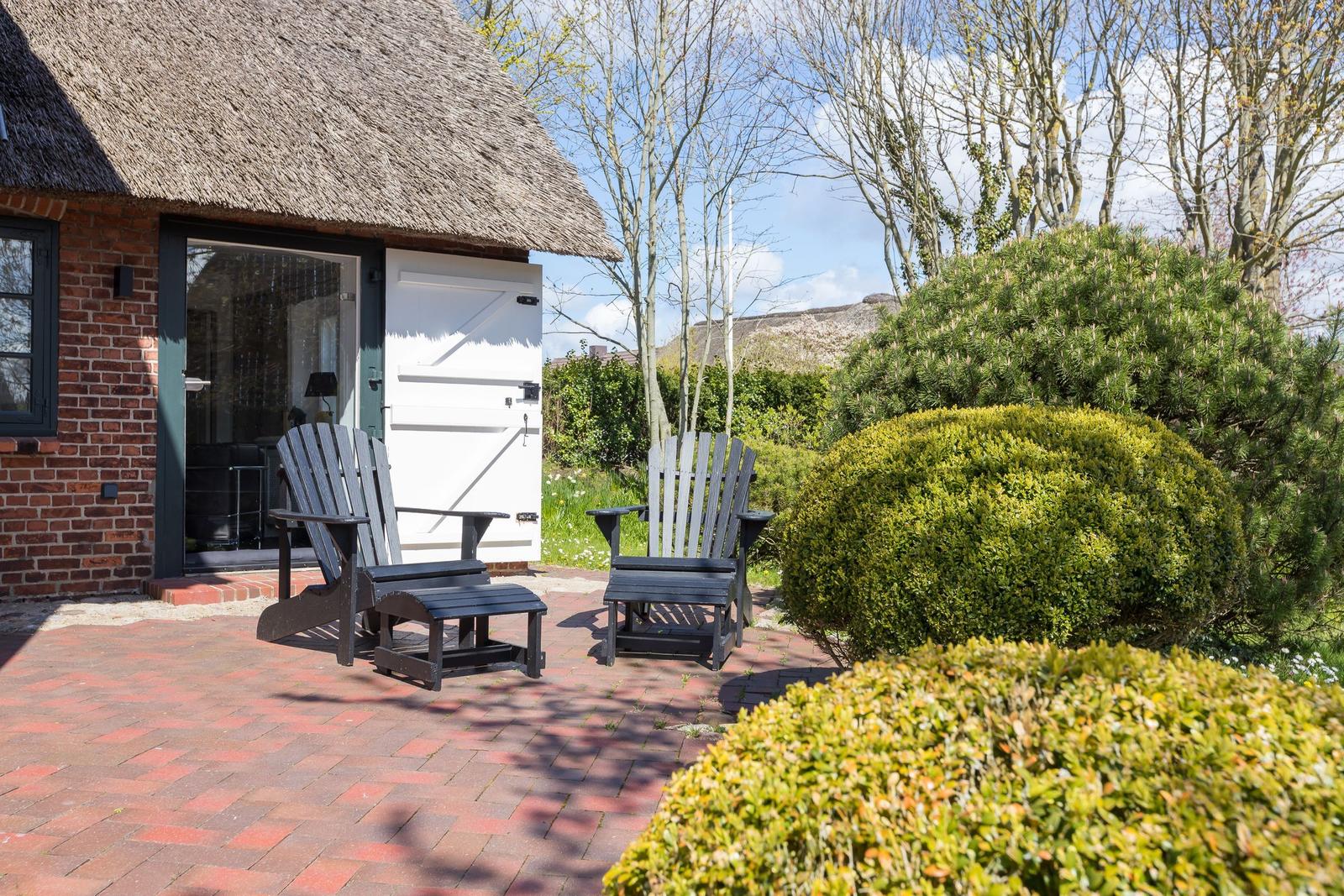 Terrasse mit zwei schwarzen Sitzgelegenheiten vor einem Haus mit Strohdach und Ziegelfassade.