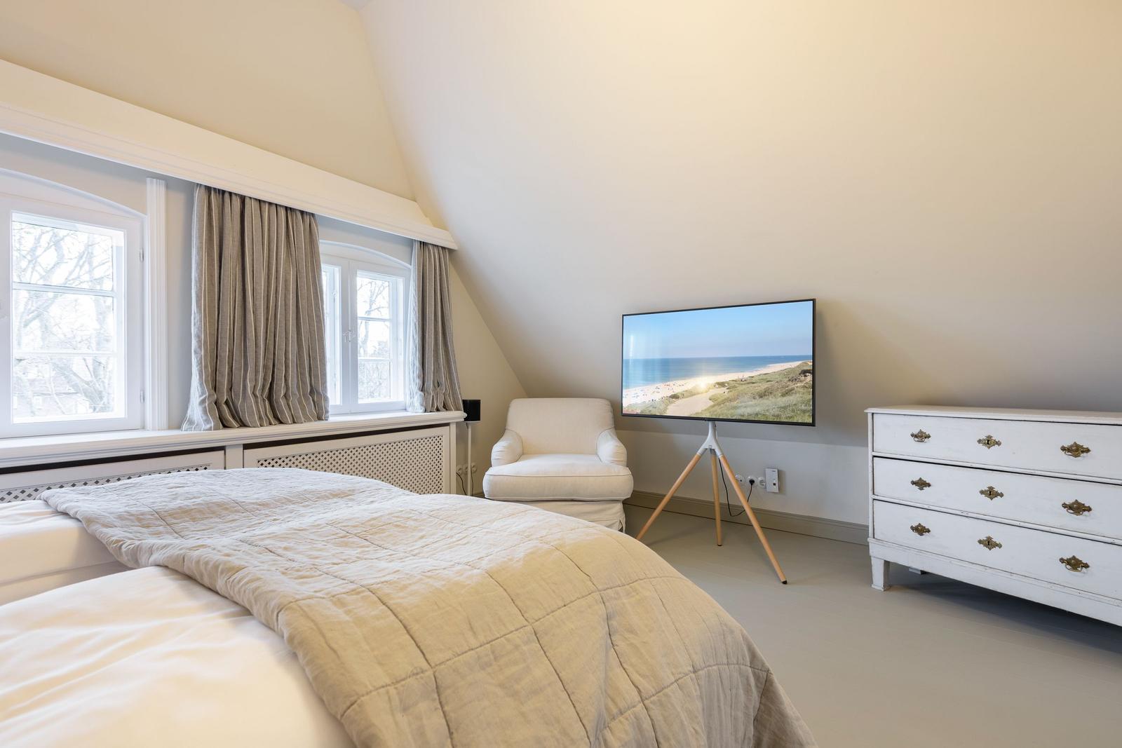 Schlafzimmer mit Bett, Fenster, Sessel, TV und Schrank.