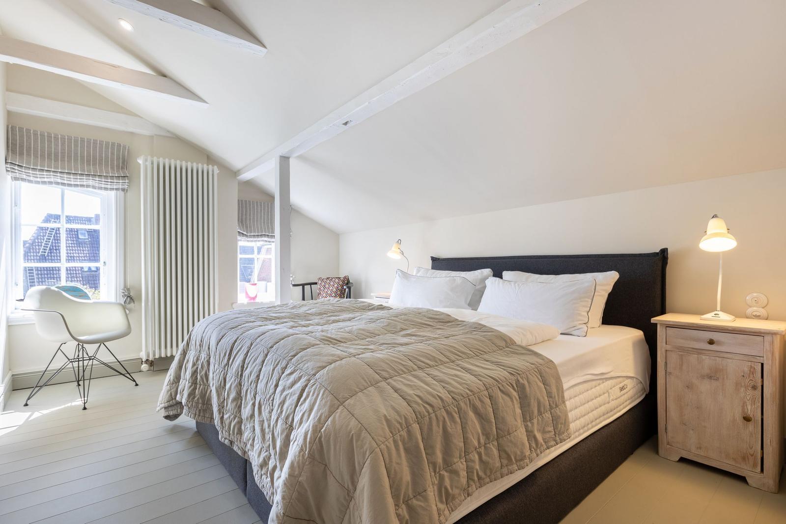Schlafzimmer mit Bett, Nachttisch und Fenster. Holzdecke mit Balken.