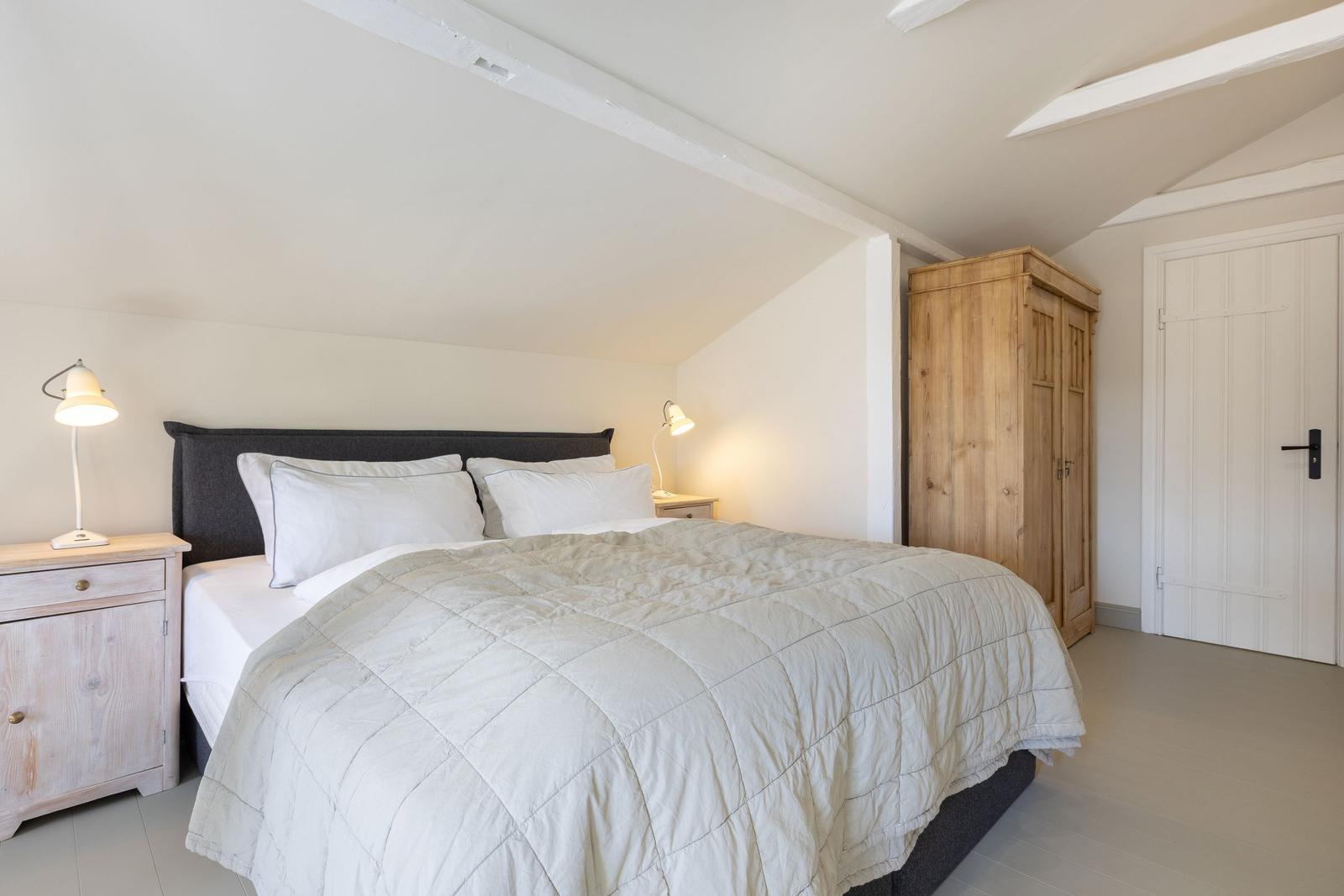 Schlafzimmer mit Bett, Nachttischen und Holzschrank unter schrägen Decken.