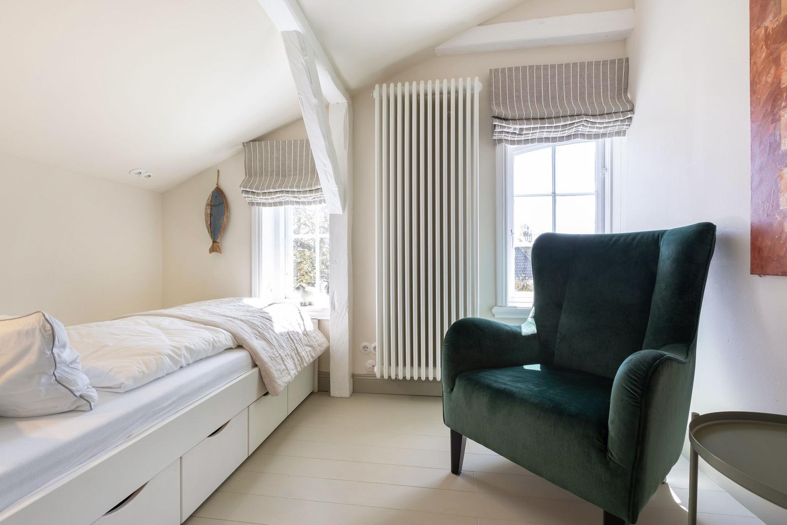Schlafzimmer mit Bett, grüner Sessel und Fenster mit Rollladen.