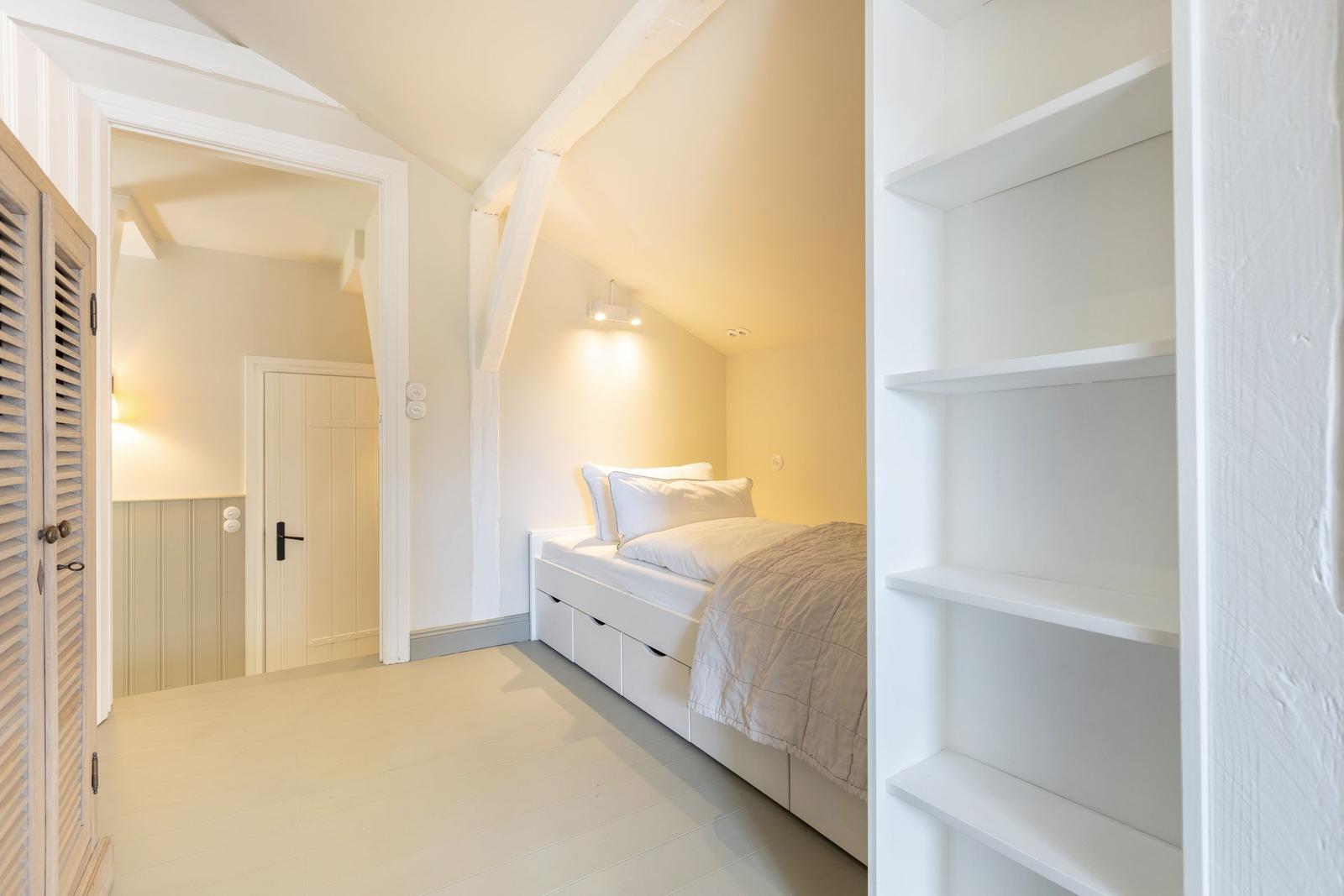 Schlafzimmer mit Dachschrägen, weißem Bett und integriertem Schrank.