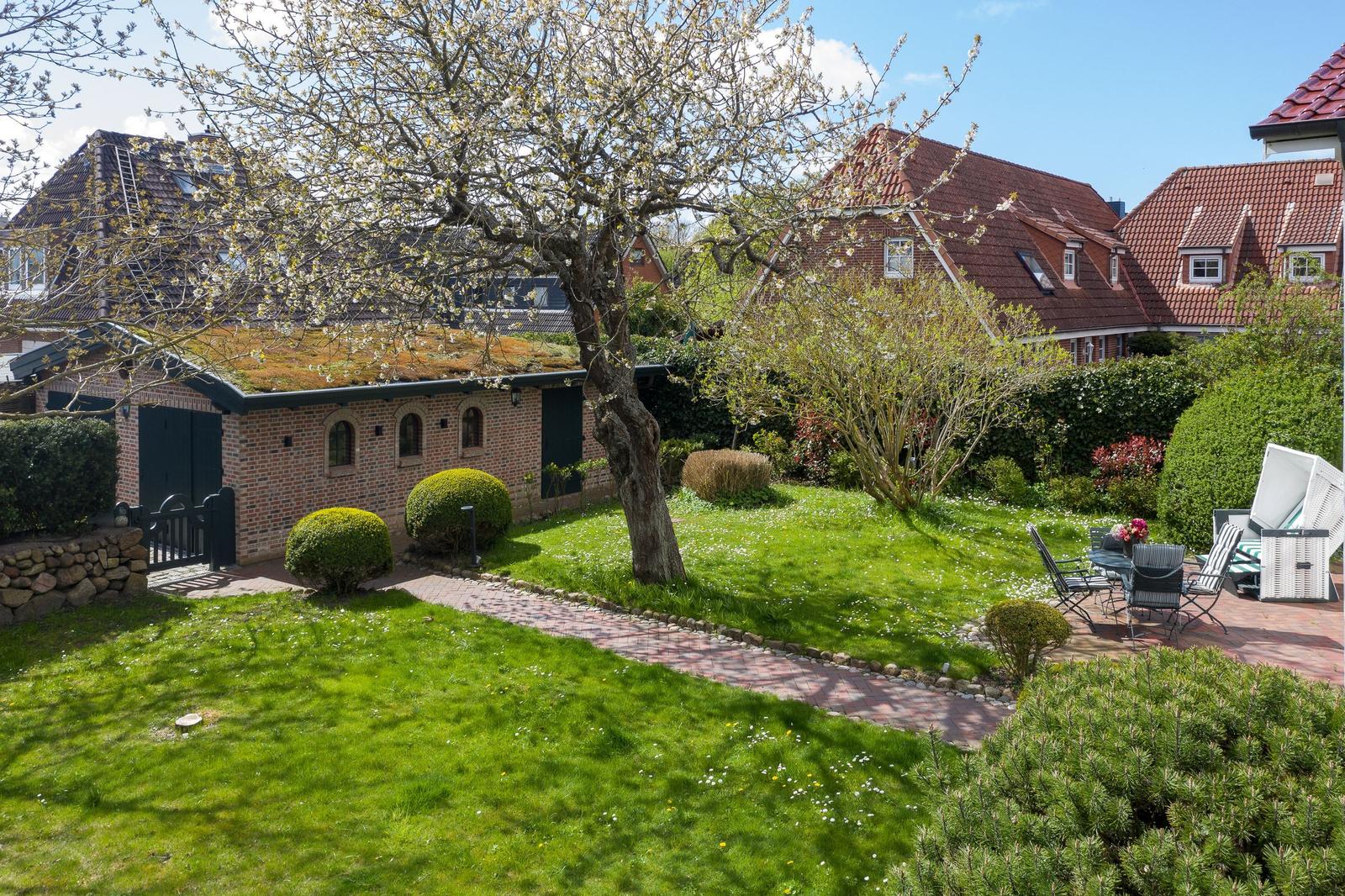 Garten mit Rasen, Weg und Sitzgelegenheit vor einem Haus mit Dachgarten.