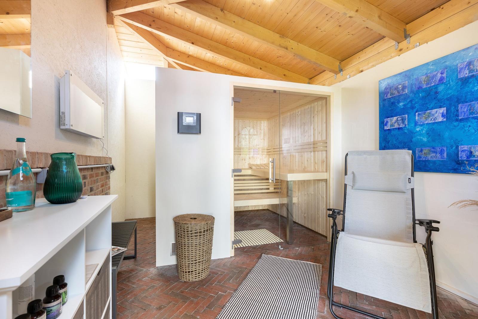 Sauna mit Glaswand, Liegestuhl und Wandbild. Holzdecke und Fliesenboden.