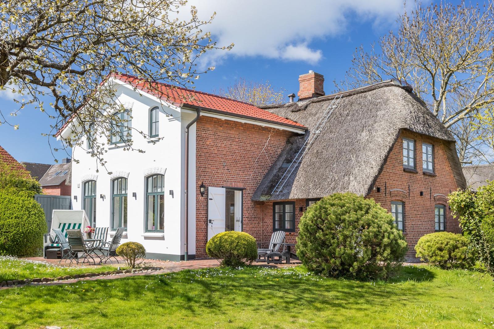 Haus mit strohgedecktem Dach und Garten mit Sitzgelegenheiten.