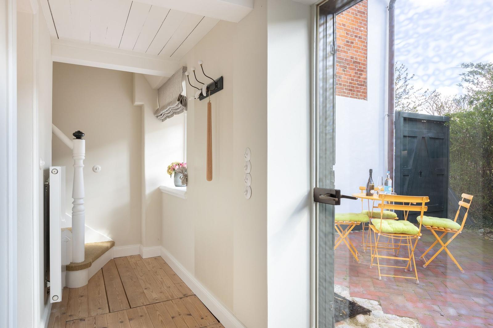 Hallway with wooden floor and stairs. Glass door leads to terrace with table and chairs.