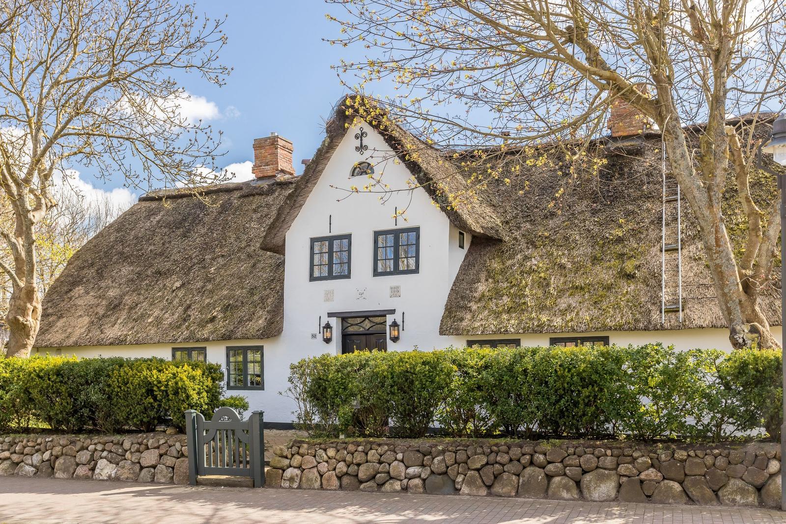 House with thatched roof, white walls, green hedges, and stone wall.