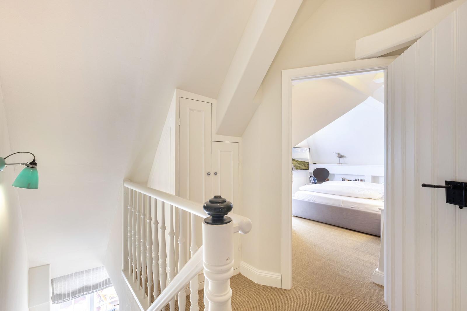 Staircase with view into bedroom with bed and wall art.