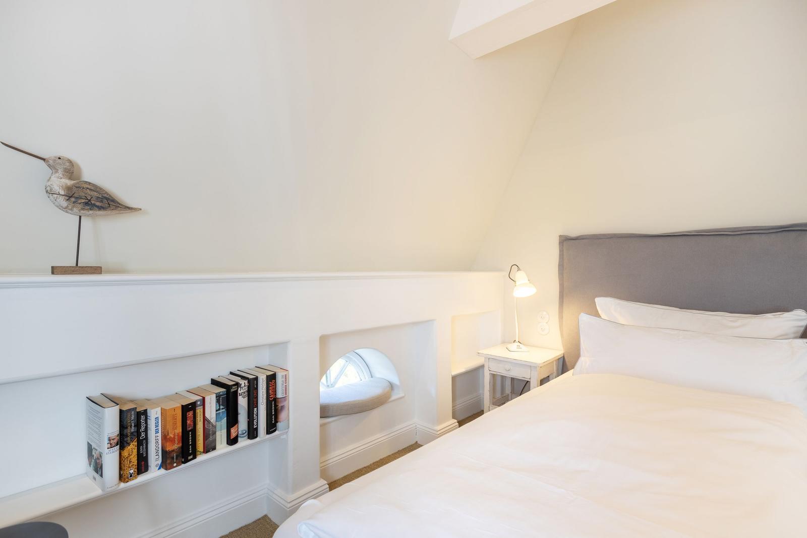 Bedroom with bed, nightstand, bookshelf, and seating nook under sloped ceiling.