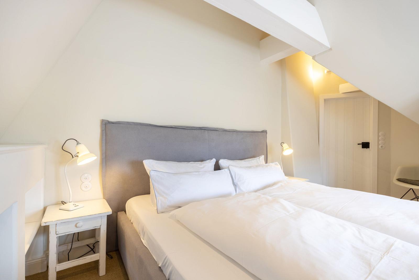 Bedroom with double bed, nightstand, and lamp under sloped ceiling.