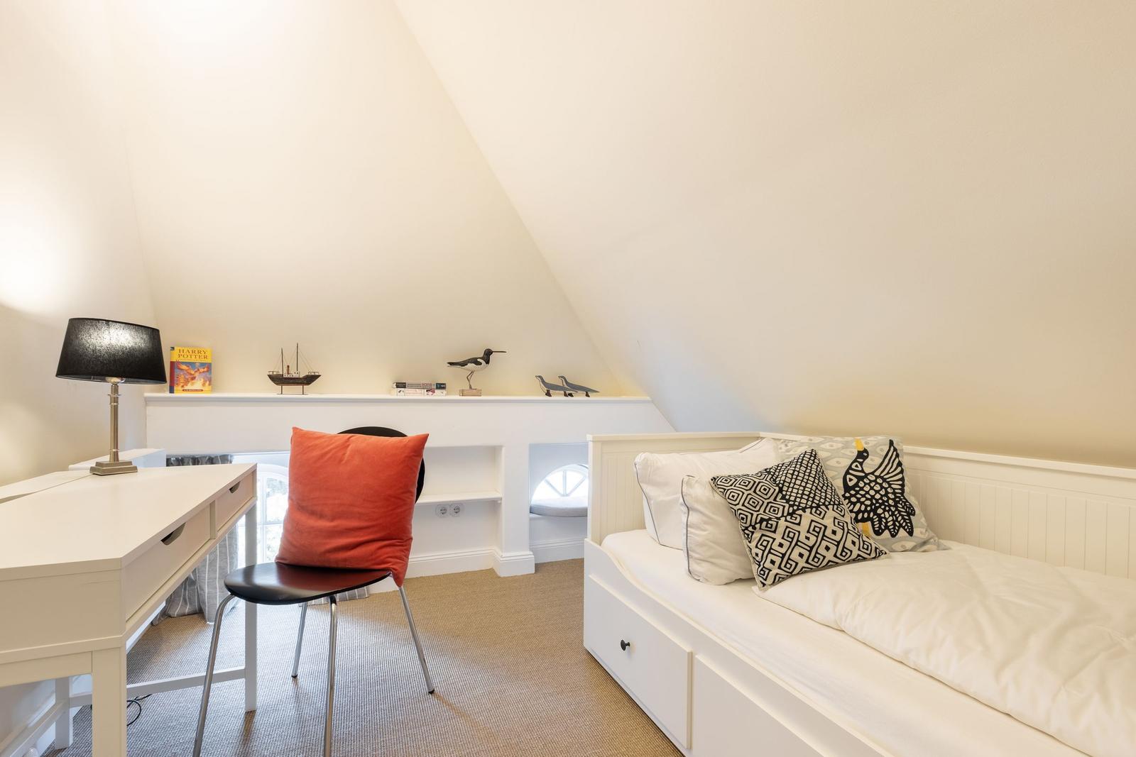 Bedroom with bed, desk, and wall shelf under sloped ceiling.