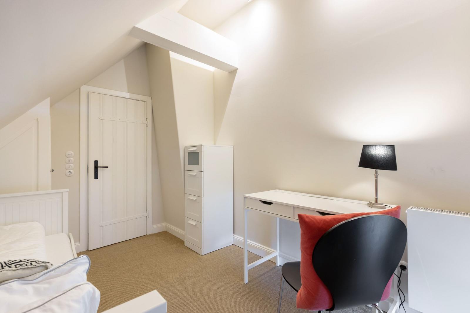 Bedroom with desk, chair, and cabinet under sloped ceiling.