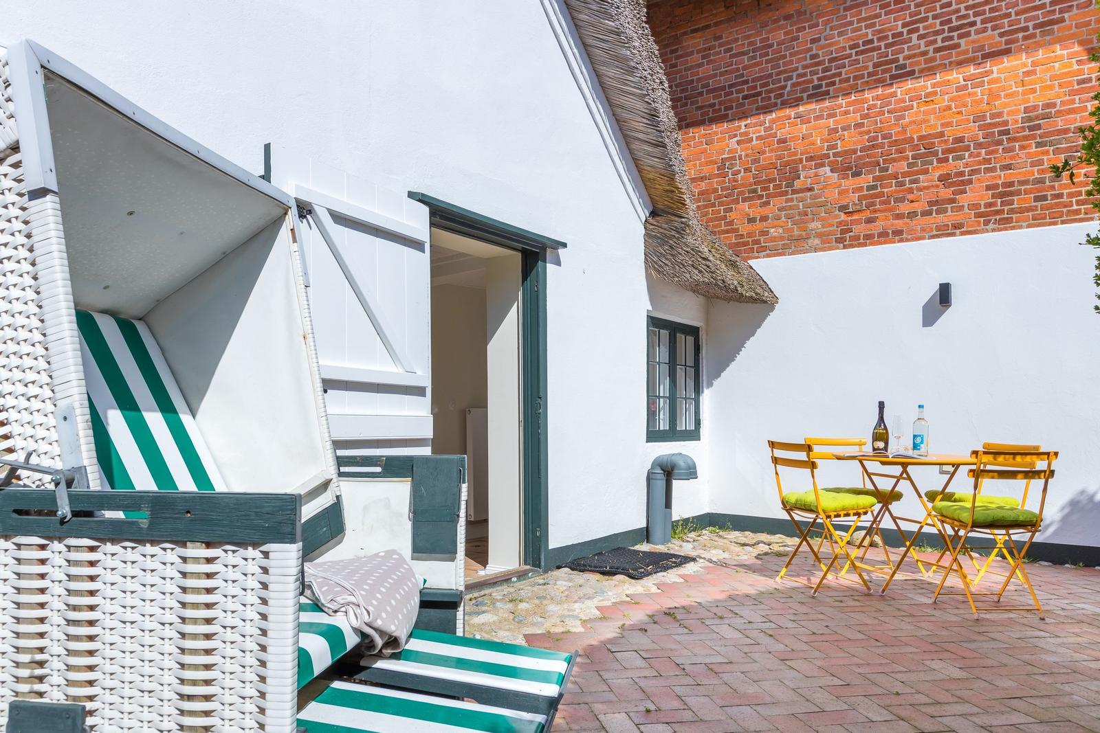 Outdoor area with beach chair, table and chairs in front of white house wall with roof
